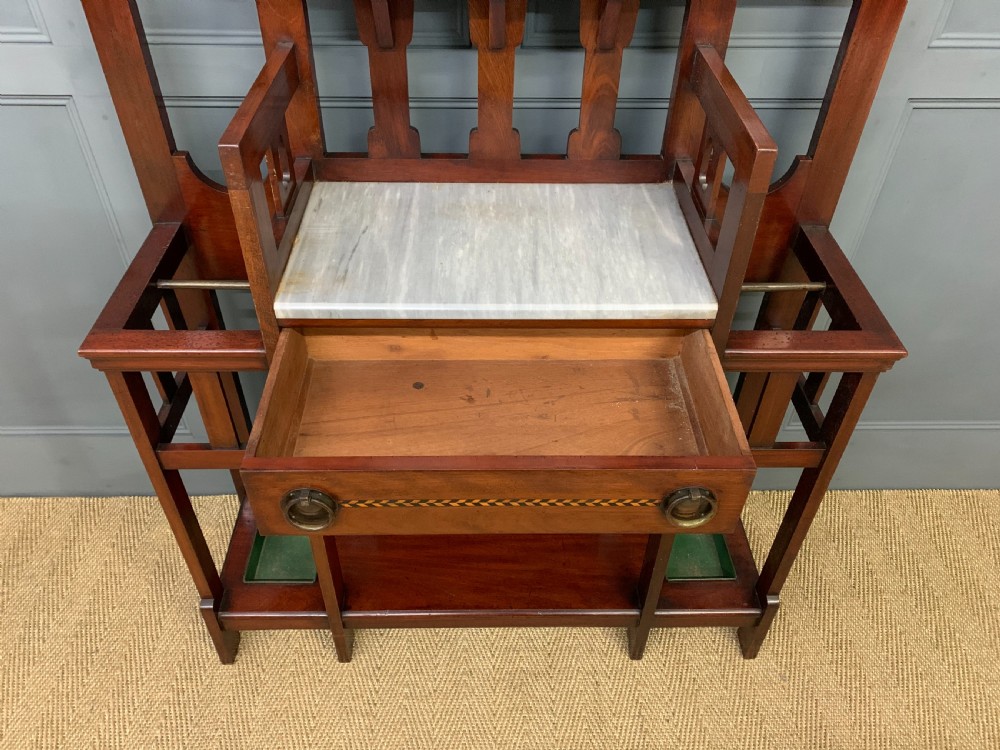 An Arts and Crafts inlaid mahogany hall stand featuring an arched central mirror, coat pegs, marble surface, and integrated umbrella racks. View VII
