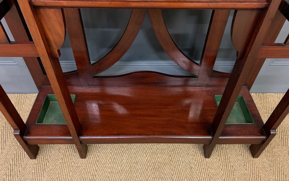 An Arts and Crafts inlaid mahogany hall stand featuring an arched central mirror, coat pegs, marble surface, and integrated umbrella racks. View X
