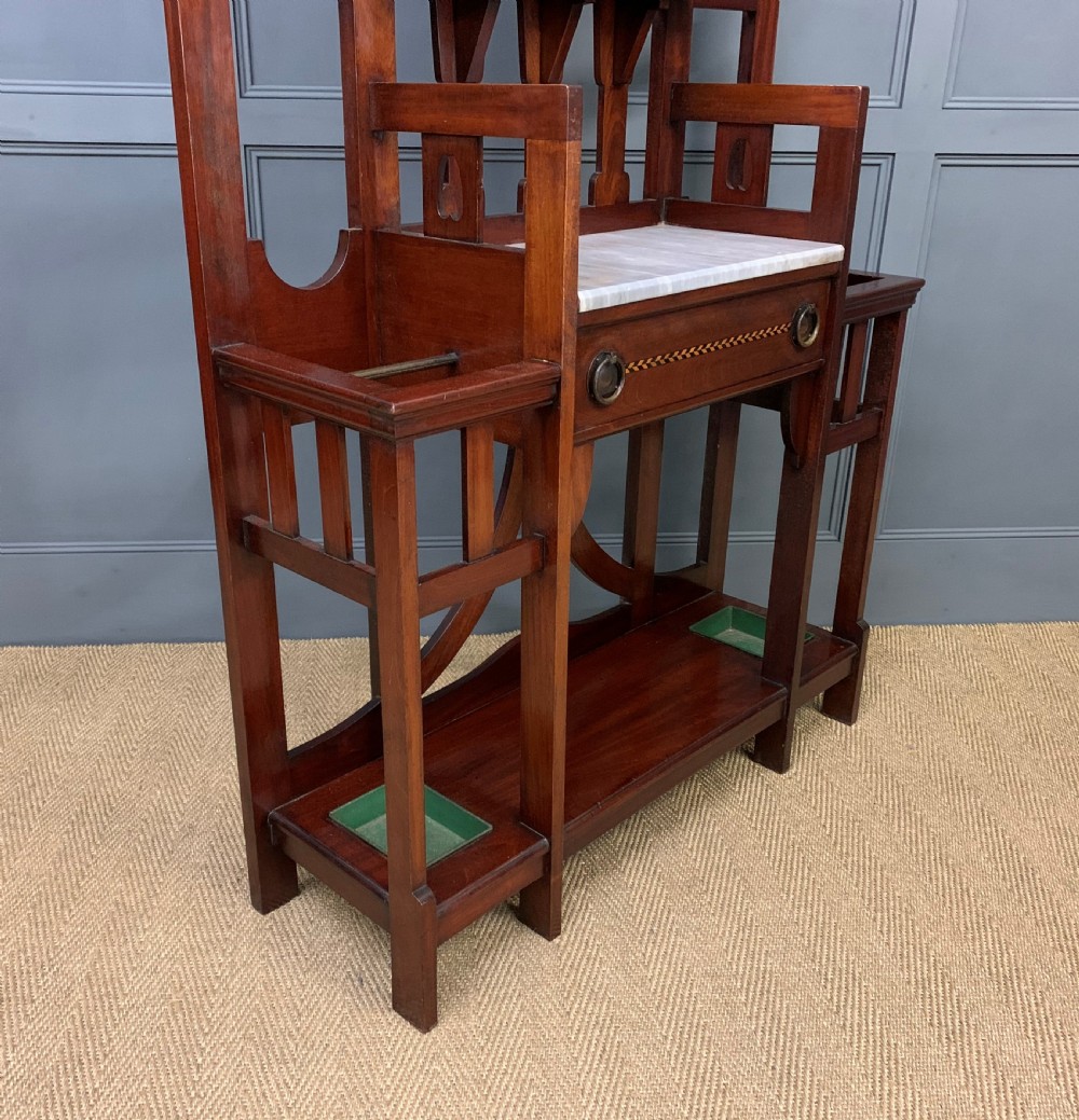 An Arts and Crafts inlaid mahogany hall stand featuring an arched central mirror, coat pegs, marble surface, and integrated umbrella racks. View XII