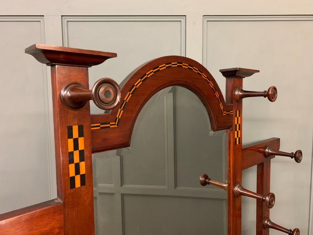An Arts and Crafts inlaid mahogany hall stand featuring an arched central mirror, coat pegs, marble surface, and integrated umbrella racks. View XIII