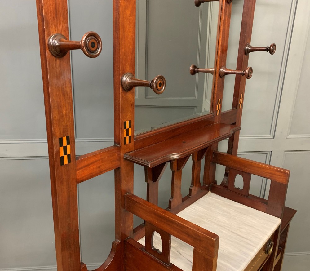 An Arts and Crafts inlaid mahogany hall stand featuring an arched central mirror, coat pegs, marble surface, and integrated umbrella racks. View XIV