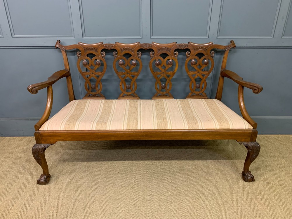 A carved mahogany Chippendale style settee featuring four pierced splats, scrolled arms, a striped fabric seat, and ball-and-claw feet. View IV