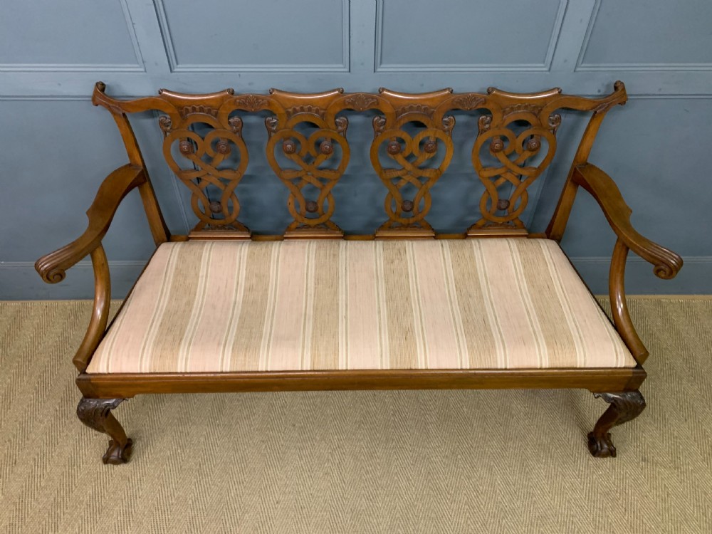 A carved mahogany Chippendale style settee featuring four pierced splats, scrolled arms, a striped fabric seat, and ball-and-claw feet. View VI