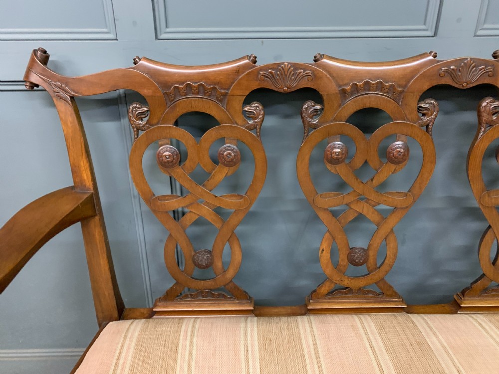 A carved mahogany Chippendale style settee featuring four pierced splats, scrolled arms, a striped fabric seat, and ball-and-claw feet. View VII