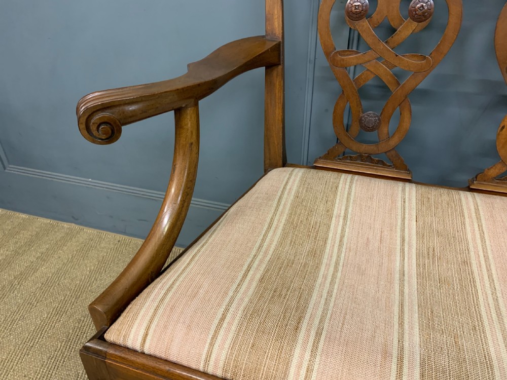 A carved mahogany Chippendale style settee featuring four pierced splats, scrolled arms, a striped fabric seat, and ball-and-claw feet. View XII
