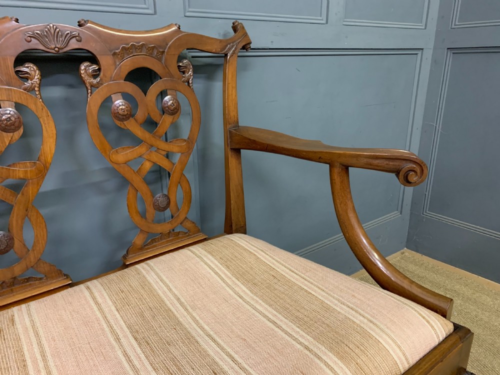 A carved mahogany Chippendale style settee featuring four pierced splats, scrolled arms, a striped fabric seat, and ball-and-claw feet. View XIV