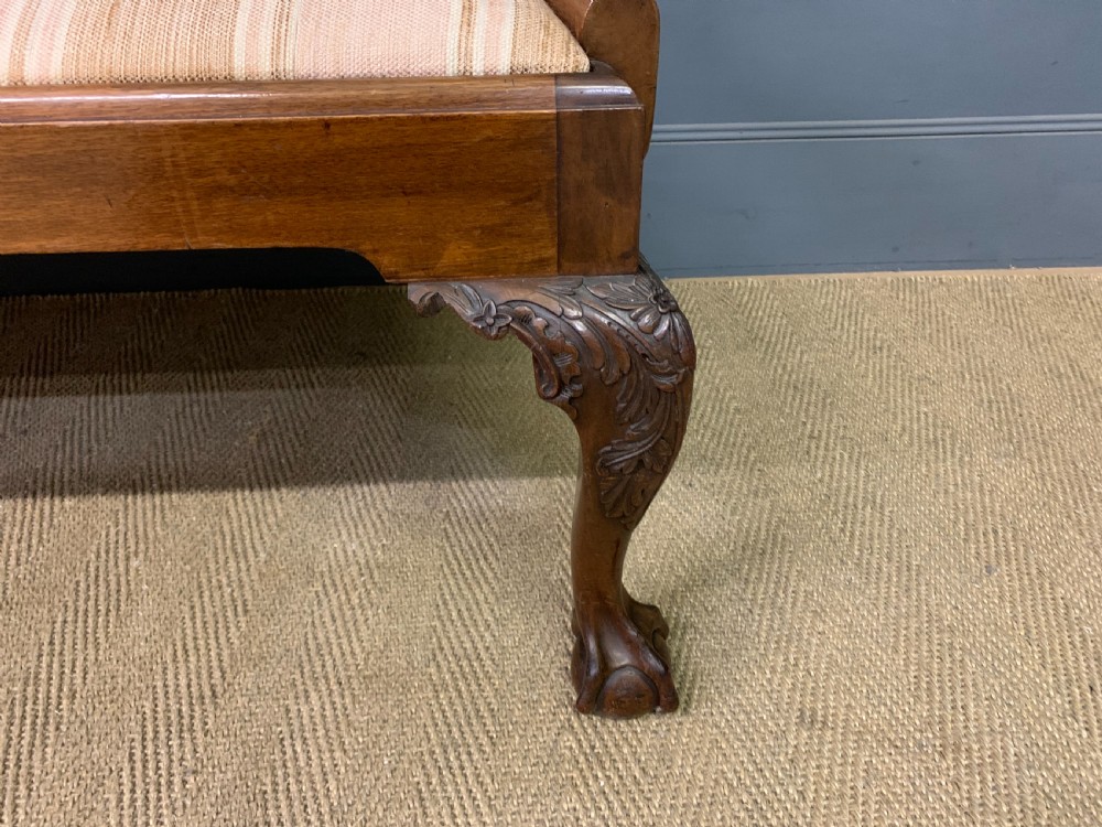 A carved mahogany Chippendale style settee featuring four pierced splats, scrolled arms, a striped fabric seat, and ball-and-claw feet. View XV