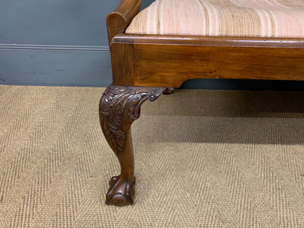 A carved mahogany Chippendale style settee featuring four pierced splats, scrolled arms, a striped fabric seat, and ball-and-claw feet. View XVI