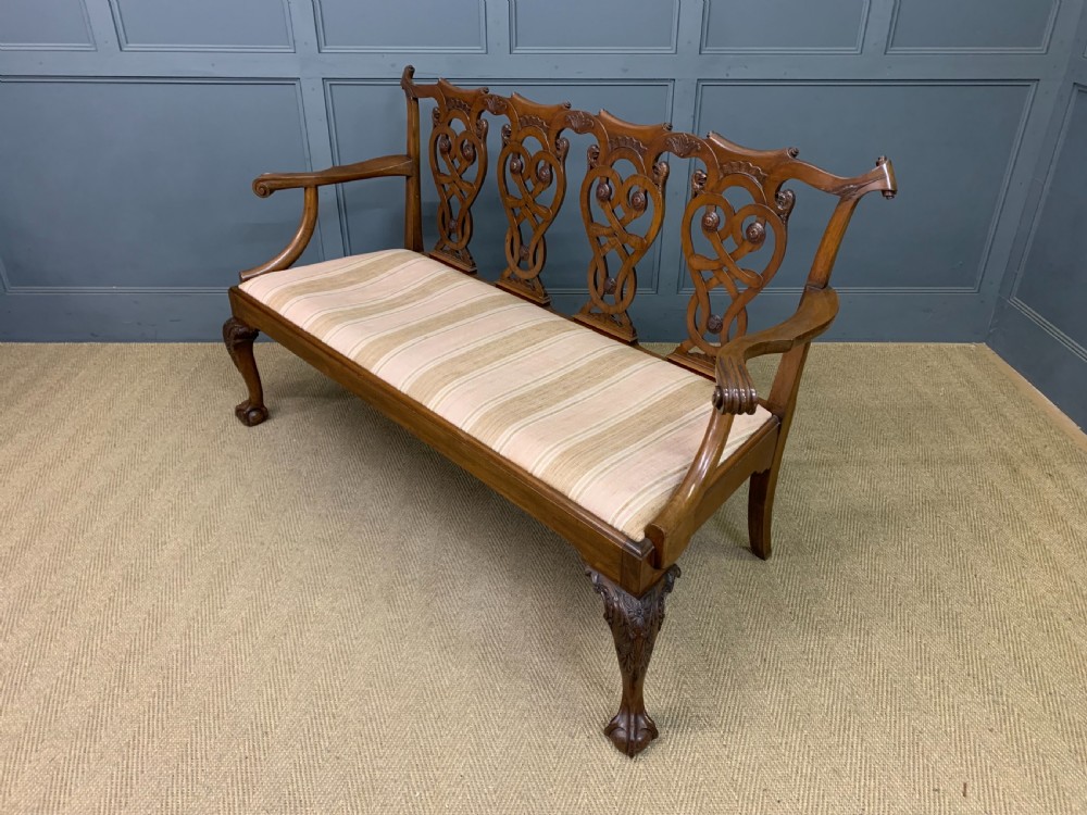 A carved mahogany Chippendale style settee featuring four pierced splats, scrolled arms, a striped fabric seat, and ball-and-claw feet. View XIX