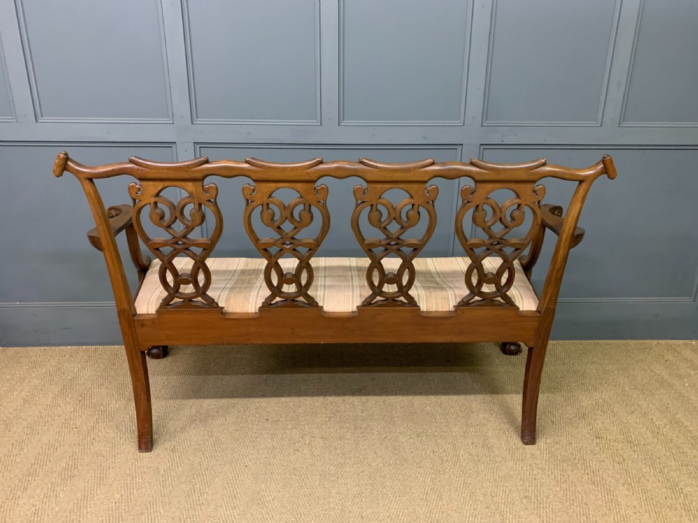A carved mahogany Chippendale style settee featuring four pierced splats, scrolled arms, a striped fabric seat, and ball-and-claw feet. View XXI