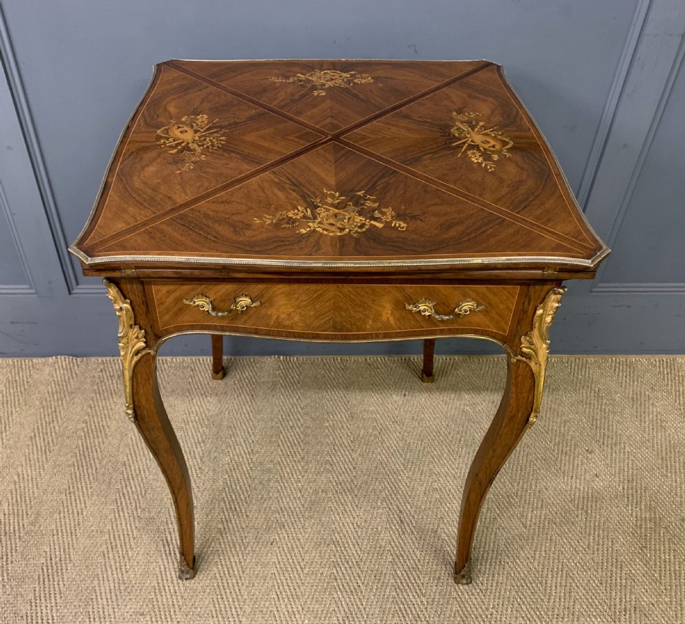 An Edwardian inlaid rosewood envelope card table featuring cabriole legs with brass mounts, a single drawer, and top flaps decorated with floral and musical instrument marquetry.