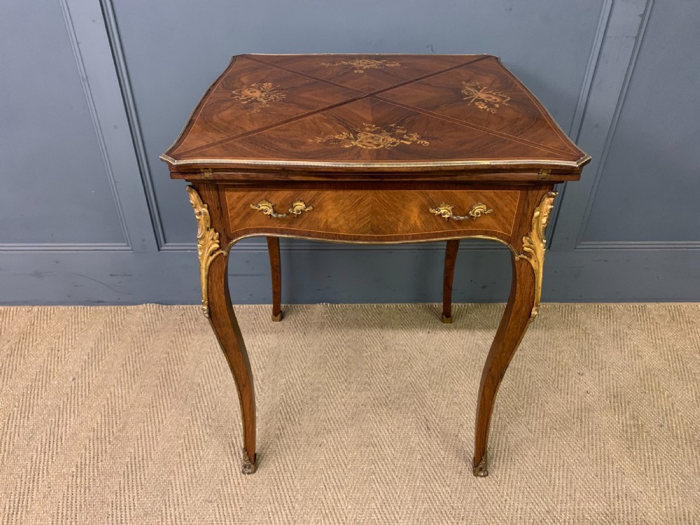 An Edwardian inlaid rosewood envelope card table featuring cabriole legs with brass mounts, a single drawer, and top flaps decorated with floral and musical instrument marquetry. View II