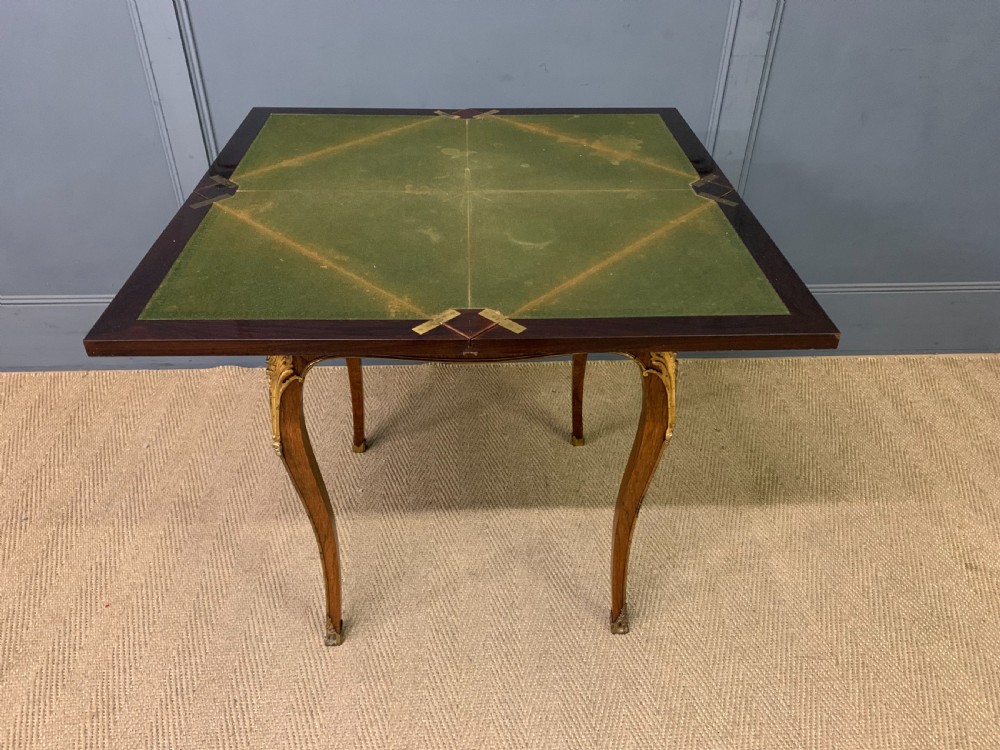 An Edwardian inlaid rosewood envelope card table featuring cabriole legs with brass mounts, a single drawer, and top flaps decorated with floral and musical instrument marquetry. View XVI