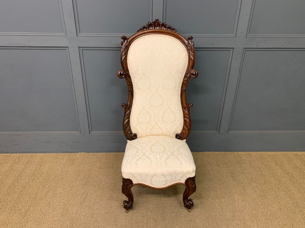 A Victorian rosewood high-back chair featuring intricately carved scrollwork, cream patterned damask upholstery, and cabriole front legs with brass castors. View II