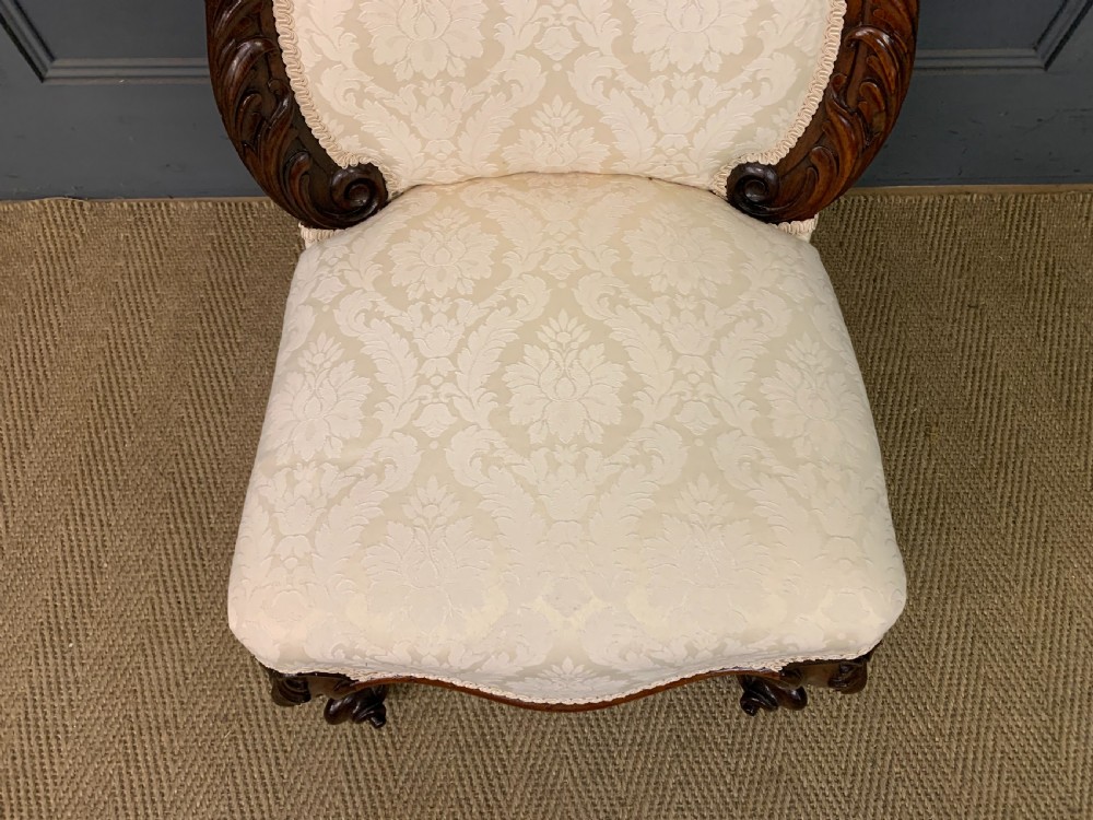 A Victorian rosewood high-back chair featuring intricately carved scrollwork, cream patterned damask upholstery, and cabriole front legs with brass castors. View III