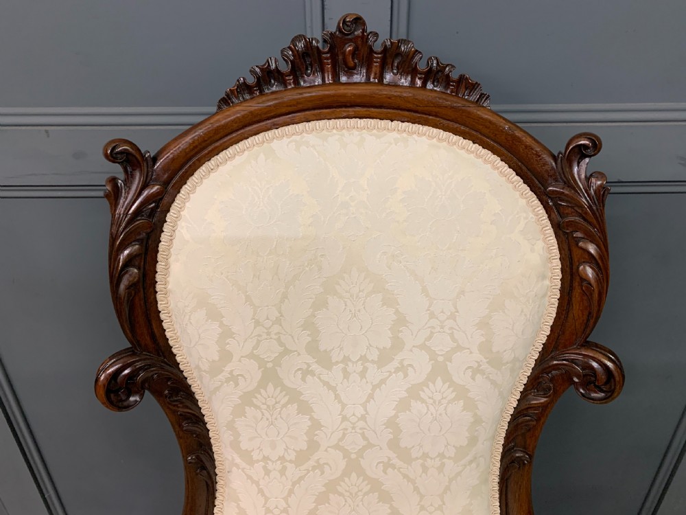 A Victorian rosewood high-back chair featuring intricately carved scrollwork, cream patterned damask upholstery, and cabriole front legs with brass castors. View IV