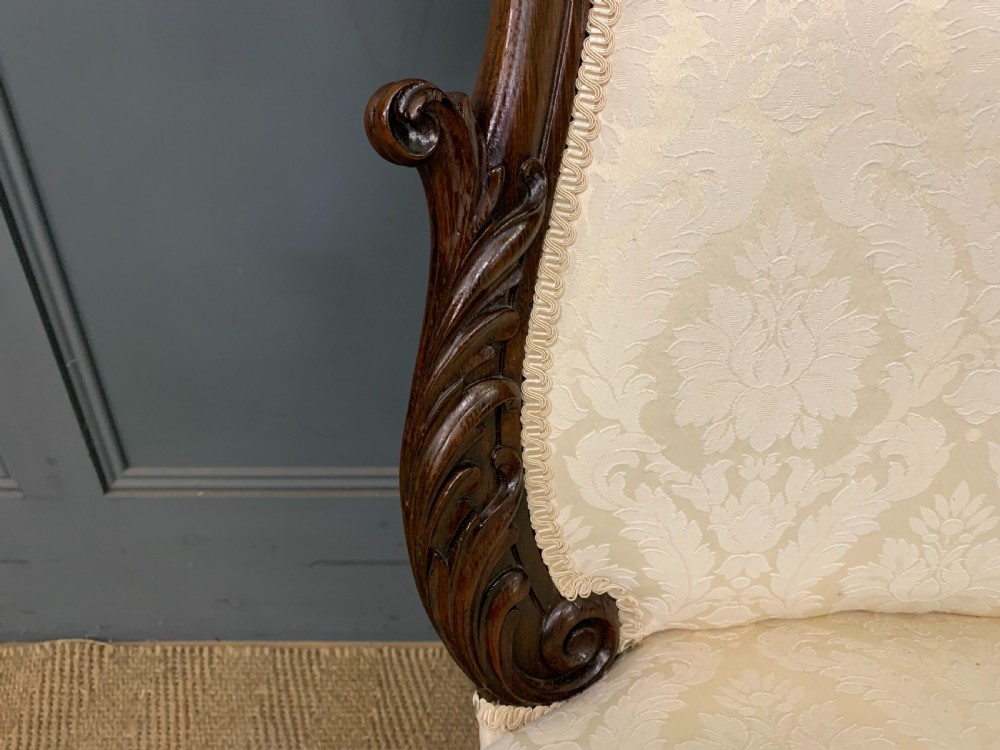A Victorian rosewood high-back chair featuring intricately carved scrollwork, cream patterned damask upholstery, and cabriole front legs with brass castors. View VII