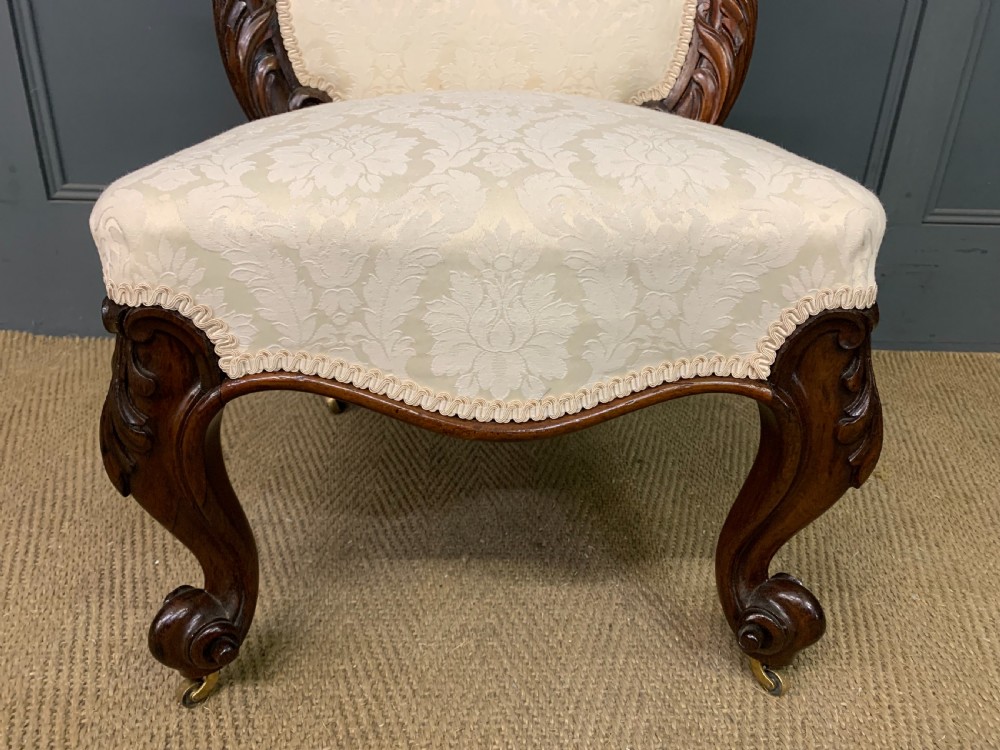 A Victorian rosewood high-back chair featuring intricately carved scrollwork, cream patterned damask upholstery, and cabriole front legs with brass castors. View VIII