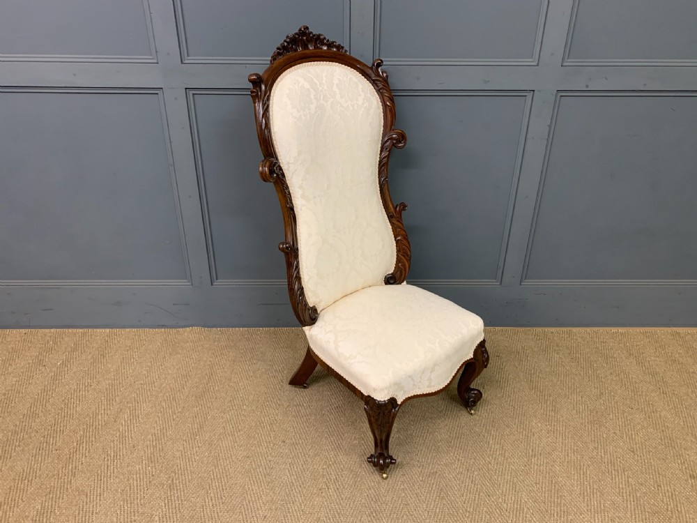A Victorian rosewood high-back chair featuring intricately carved scrollwork, cream patterned damask upholstery, and cabriole front legs with brass castors. View IX
