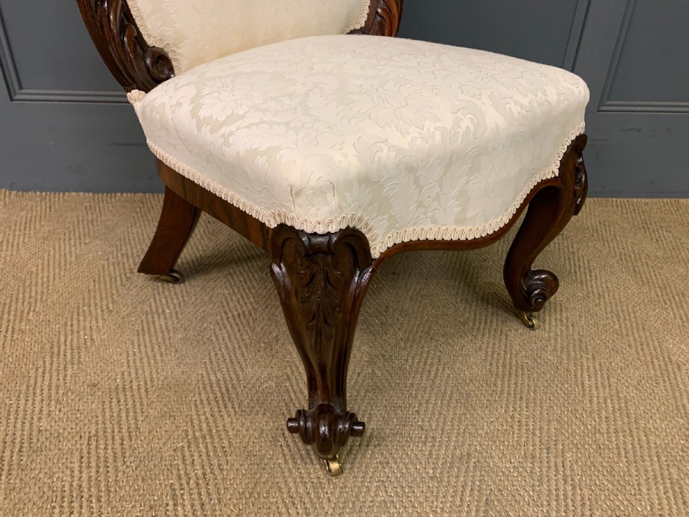 A Victorian rosewood high-back chair featuring intricately carved scrollwork, cream patterned damask upholstery, and cabriole front legs with brass castors. View X