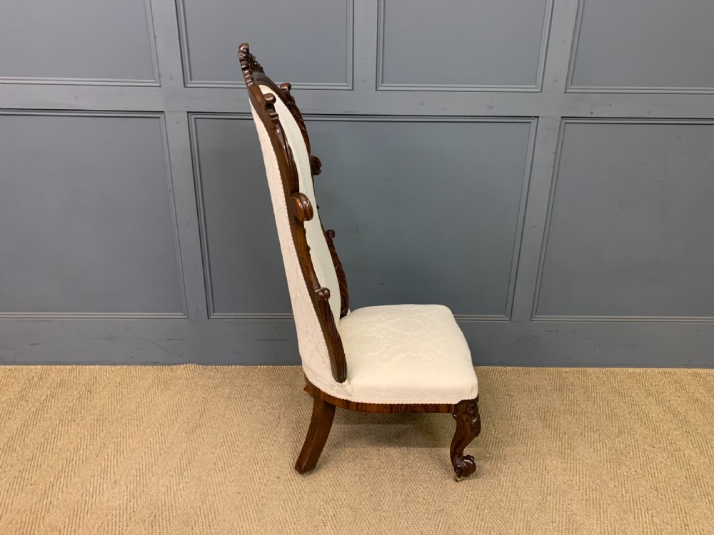 A Victorian rosewood high-back chair featuring intricately carved scrollwork, cream patterned damask upholstery, and cabriole front legs with brass castors. View XII