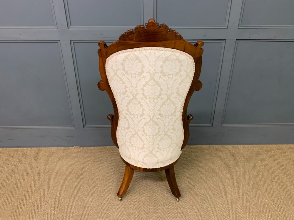 A Victorian rosewood high-back chair featuring intricately carved scrollwork, cream patterned damask upholstery, and cabriole front legs with brass castors. View XIII