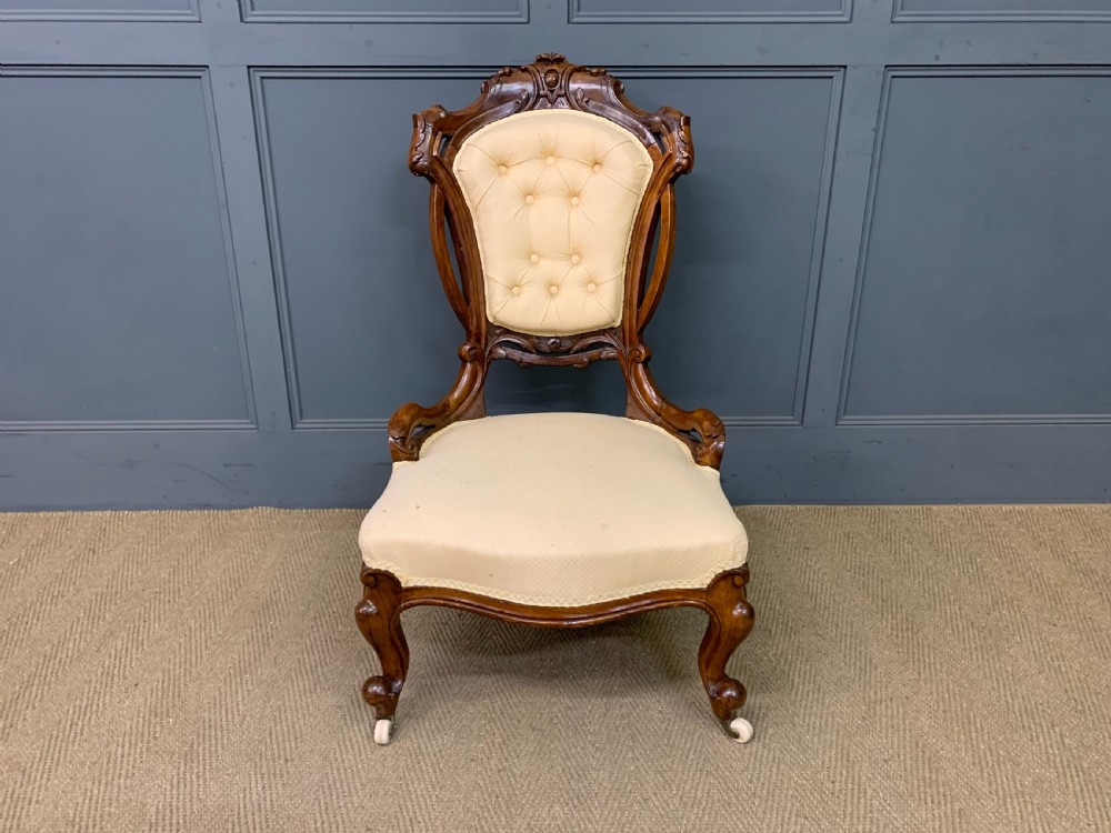A Victorian walnut salon chair featuring a button-tufted cream backrest, carved wooden frame, cabriole front legs, and ceramic castors. View II