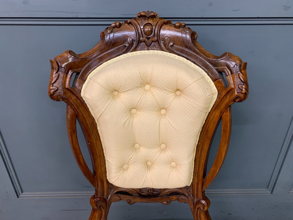 A Victorian walnut salon chair featuring a button-tufted cream backrest, carved wooden frame, cabriole front legs, and ceramic castors. View IV