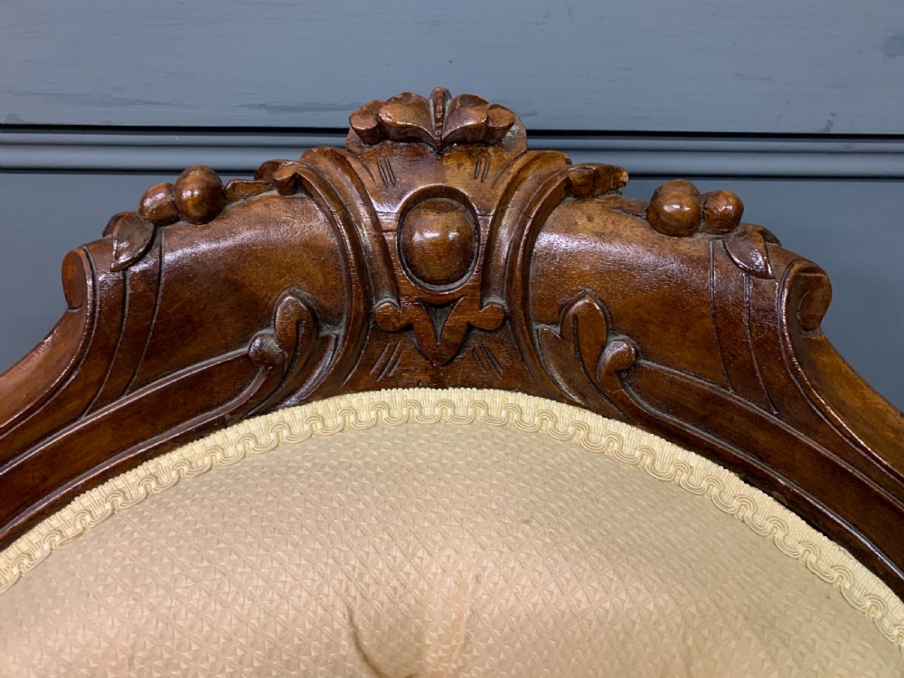 A Victorian walnut salon chair featuring a button-tufted cream backrest, carved wooden frame, cabriole front legs, and ceramic castors. View V