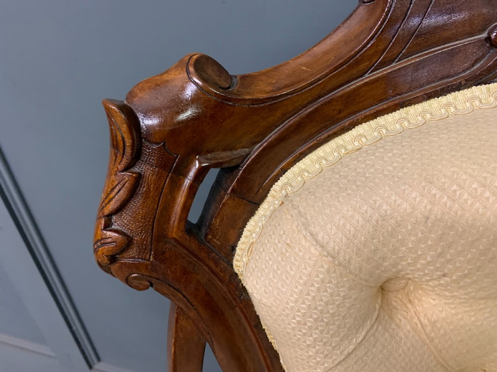 A Victorian walnut salon chair featuring a button-tufted cream backrest, carved wooden frame, cabriole front legs, and ceramic castors. View VI
