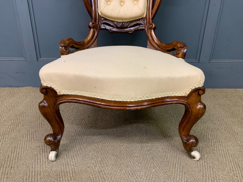 A Victorian walnut salon chair featuring a button-tufted cream backrest, carved wooden frame, cabriole front legs, and ceramic castors. View IX
