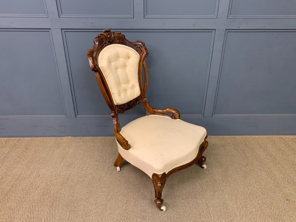 A Victorian walnut salon chair featuring a button-tufted cream backrest, carved wooden frame, cabriole front legs, and ceramic castors. View X