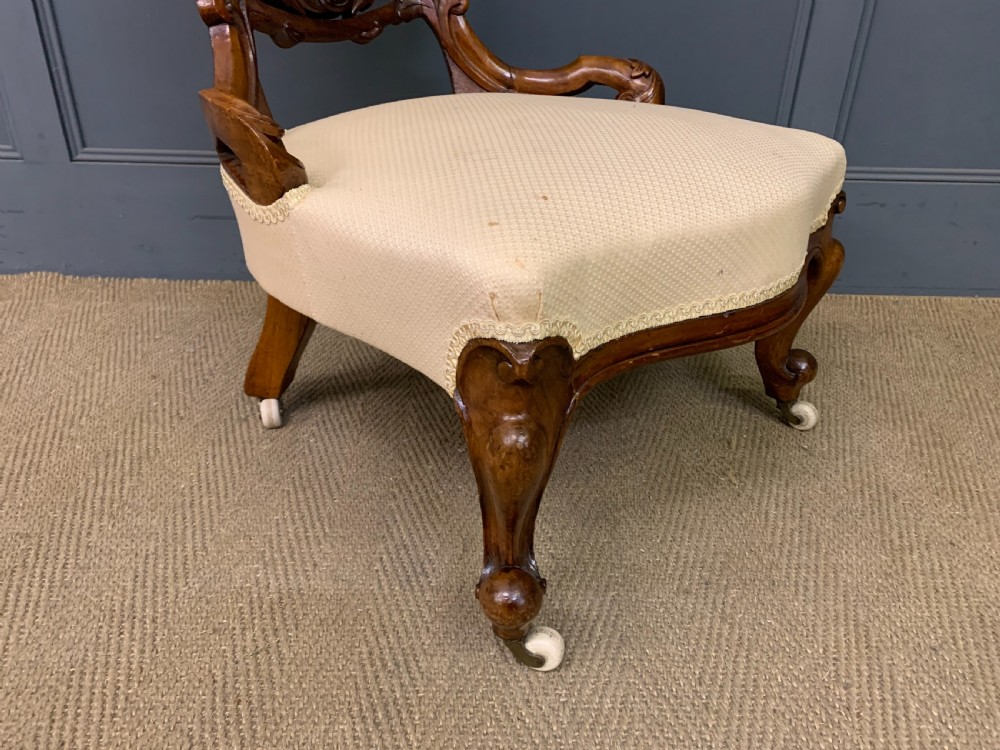 A Victorian walnut salon chair featuring a button-tufted cream backrest, carved wooden frame, cabriole front legs, and ceramic castors. View XI
