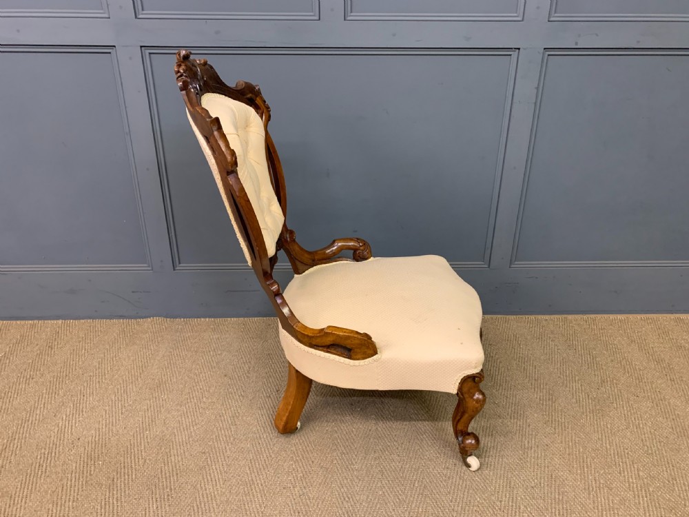 A Victorian walnut salon chair featuring a button-tufted cream backrest, carved wooden frame, cabriole front legs, and ceramic castors. View XII