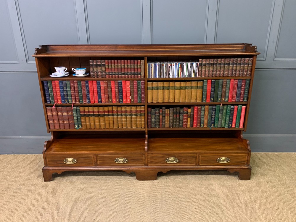 A wide Edwardian mahogany open bookcase with two multi-tiered shelving sections above four drawers with brass handles.