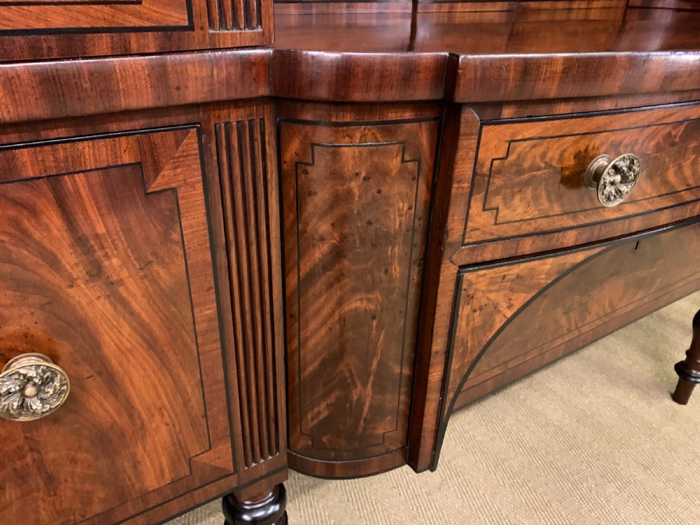A Regency period flame mahogany sideboard featuring a raised stage top, central drawer, two side cupboards, detailed stringing, and turned reeded legs. View XI