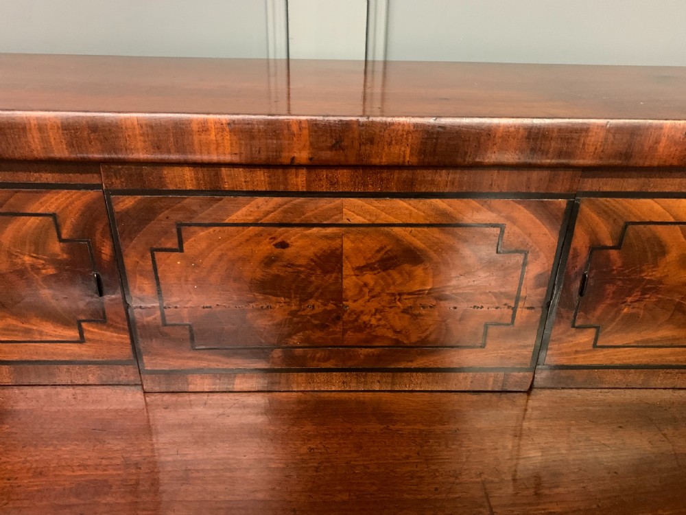A Regency period flame mahogany sideboard featuring a raised stage top, central drawer, two side cupboards, detailed stringing, and turned reeded legs. View XIII
