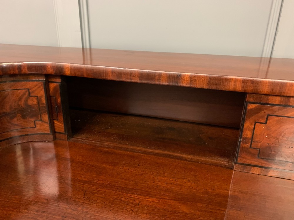 A Regency period flame mahogany sideboard featuring a raised stage top, central drawer, two side cupboards, detailed stringing, and turned reeded legs. View XVI