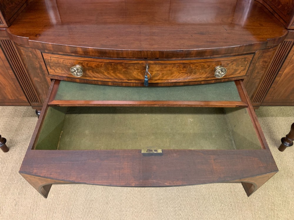 A Regency period flame mahogany sideboard featuring a raised stage top, central drawer, two side cupboards, detailed stringing, and turned reeded legs. View XXII