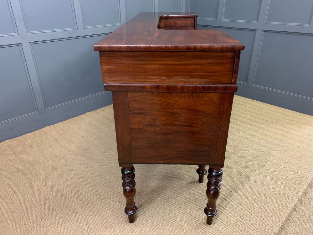 A Regency period flame mahogany sideboard featuring a raised stage top, central drawer, two side cupboards, detailed stringing, and turned reeded legs. View XXIV