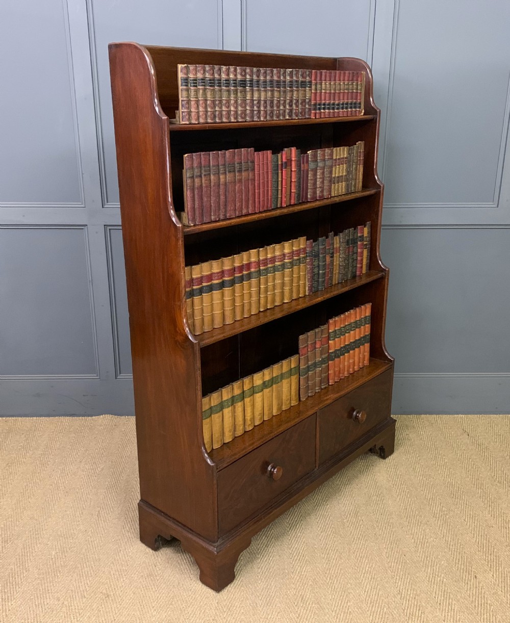 Victorian mahogany waterfall open bookcase featuring graduated shelves, shaped sides, and two lower drawers with turned wooden handles.