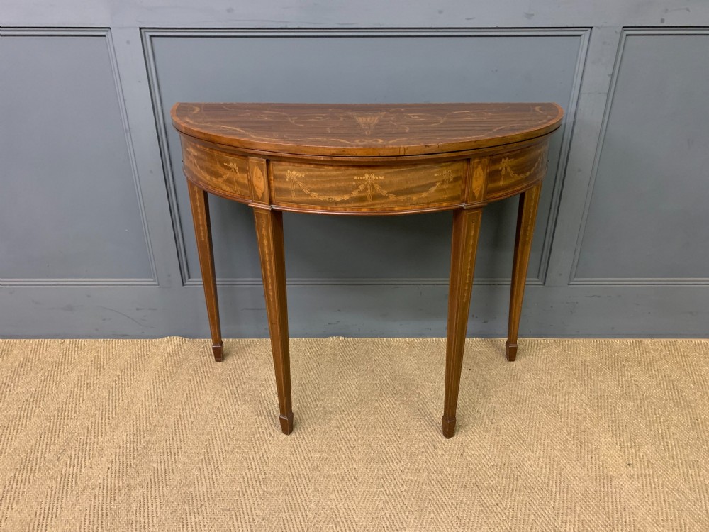 A demilune mahogany card table with floral marquetry inlays on the fold-over top and four square tapered legs. View III