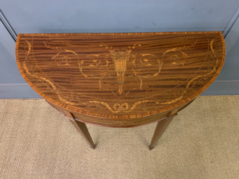 A demilune mahogany card table with floral marquetry inlays on the fold-over top and four square tapered legs. View IV