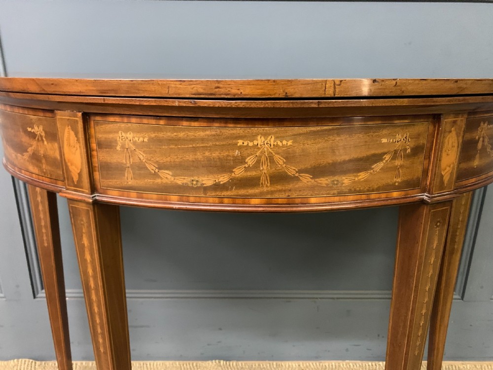 A demilune mahogany card table with floral marquetry inlays on the fold-over top and four square tapered legs. View VIII