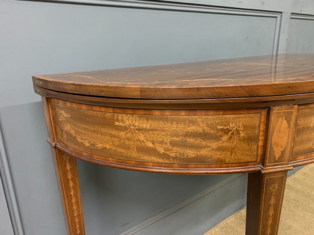 A demilune mahogany card table with floral marquetry inlays on the fold-over top and four square tapered legs. View IX