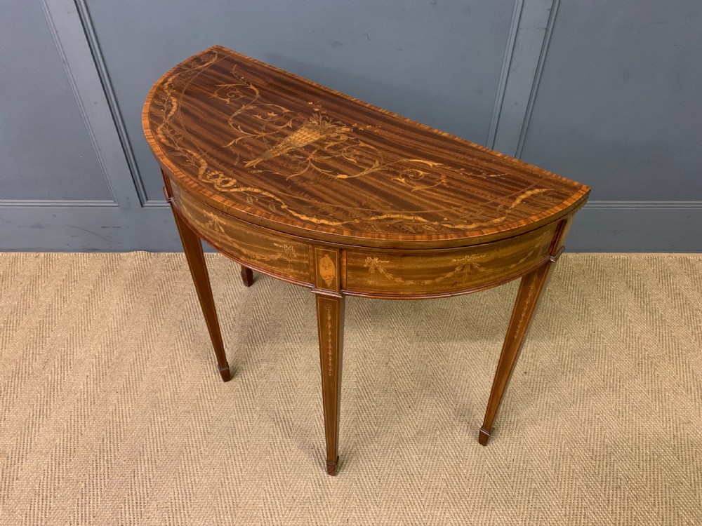 A demilune mahogany card table with floral marquetry inlays on the fold-over top and four square tapered legs. View XV