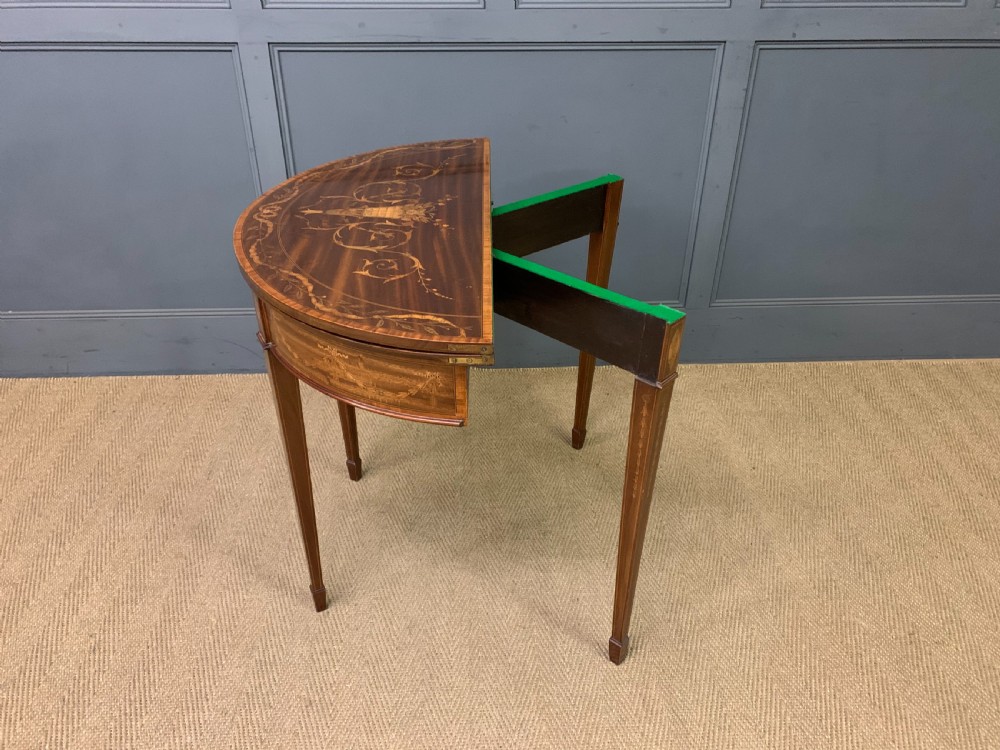 A demilune mahogany card table with floral marquetry inlays on the fold-over top and four square tapered legs. View XVI