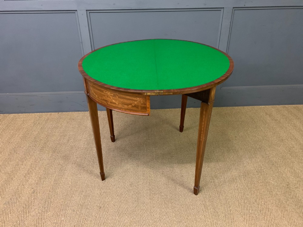 A demilune mahogany card table with floral marquetry inlays on the fold-over top and four square tapered legs. View XVII