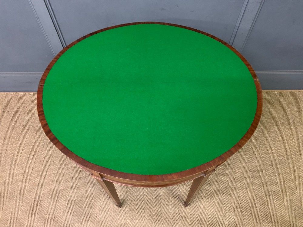 A demilune mahogany card table with floral marquetry inlays on the fold-over top and four square tapered legs. View XIX