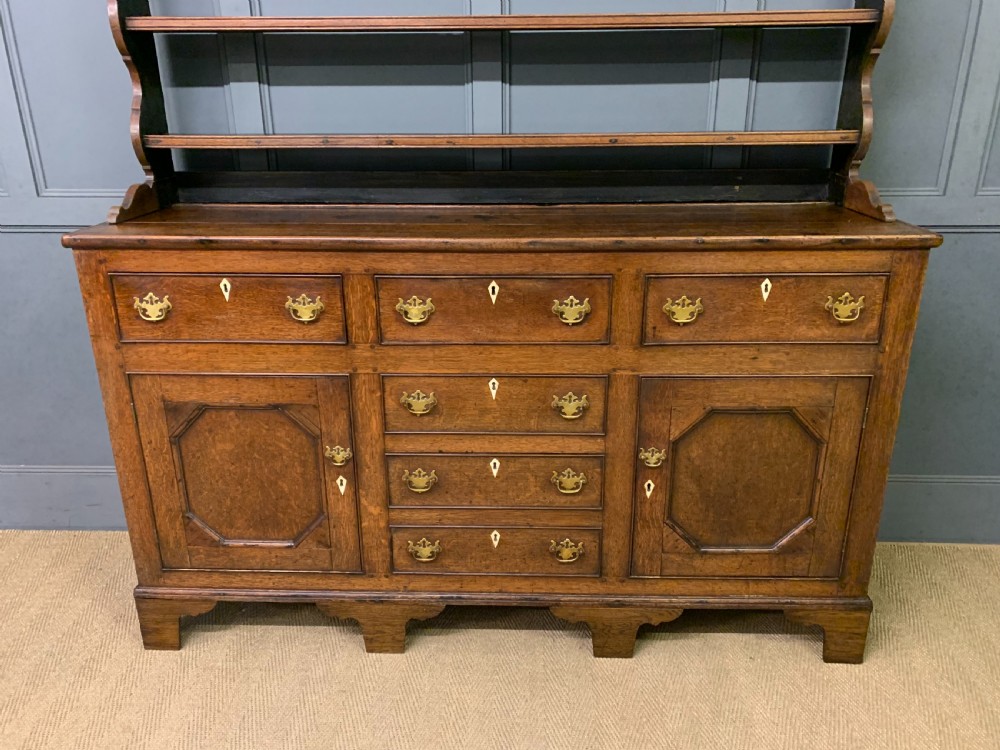 An early nineteenth-century Welsh oak dresser featuring a three-tier open plate rack above a base with drawers, cupboards, and brass hardware. View IV